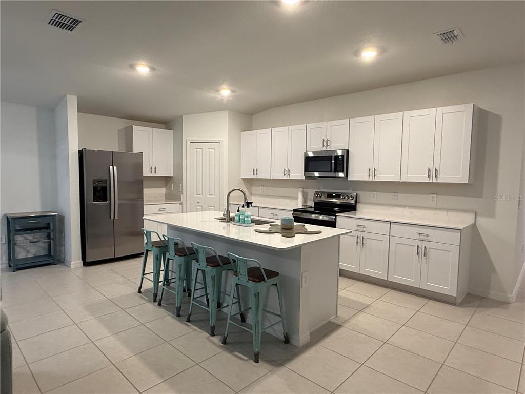 A kitchen features white cabinets, stainless steel appliances, a center island, and light tile flooring — 13038 CALCITE BLUE AVENUE, WIMAUMA, FL