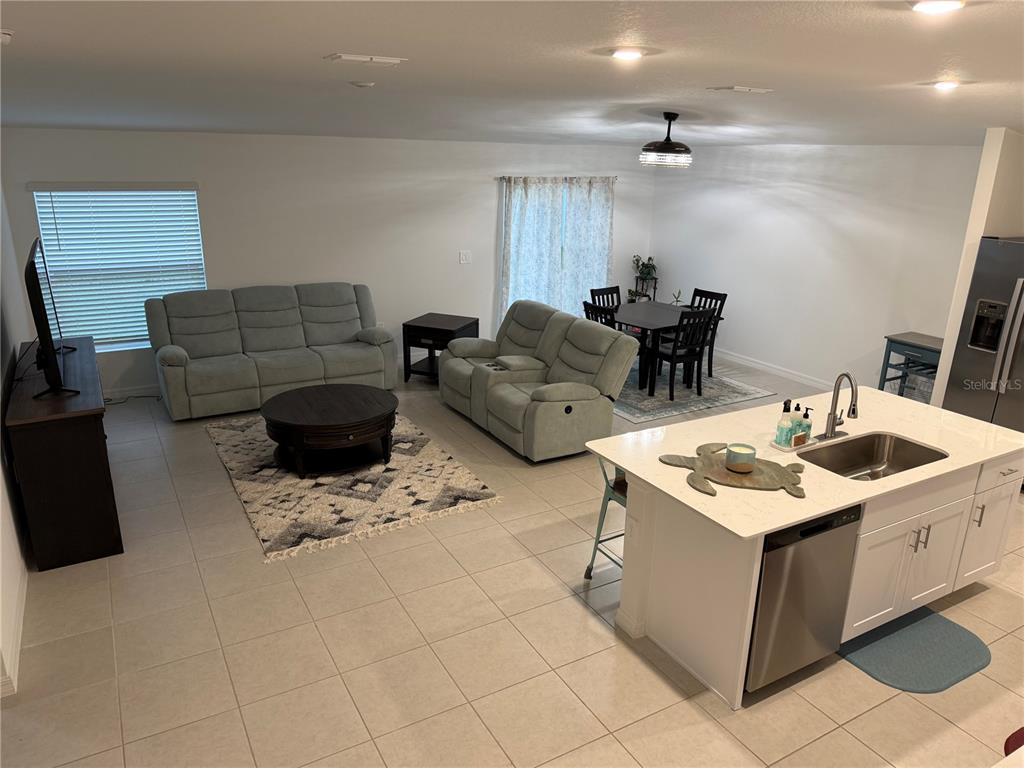 An open-concept living room and kitchen area features light-colored tile flooring and neutral walls — 13038 CALCITE BLUE AVENUE, WIMAUMA, FL
