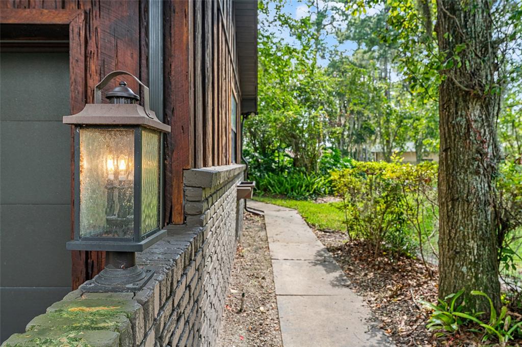 A lit outdoor lantern sits on a brick wall beside a wooden house and walkway — 8101 NW 46TH STREET, OCALA, FL