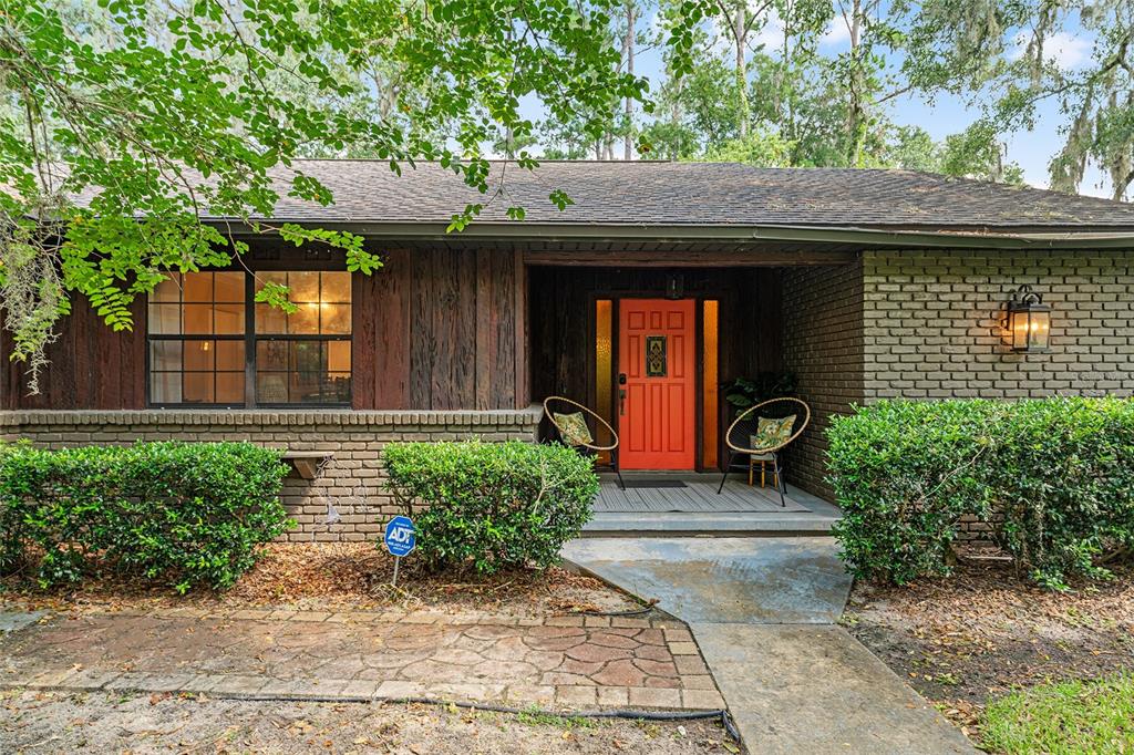 The exterior of a single-story house features a brick facade, wood siding, and a red door — 8101 NW 46TH STREET, OCALA, FL