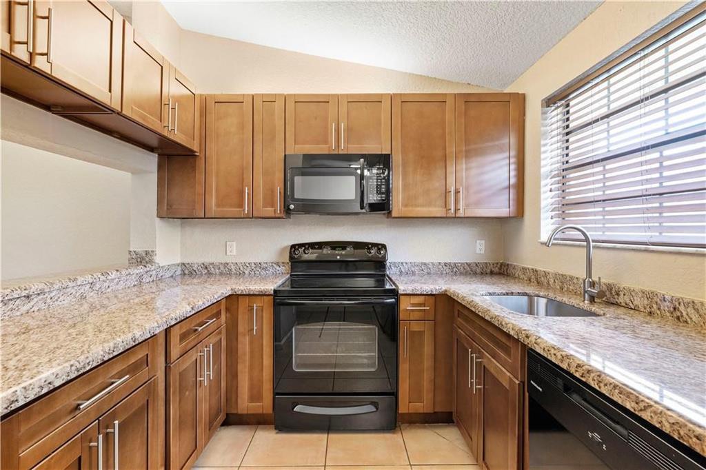 A kitchen features wood cabinets, granite countertops, and black appliances under a vaulted ceiling — 912 Congressional Way, Deerfield Beach FL 33442, DEERFIELD BEACH, FL