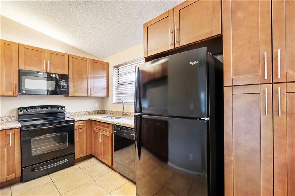 A kitchen with light wood cabinets, black appliances, granite countertops, and light-colored tile flooring — 912 Congressional Way, Deerfield Beach FL 33442, DEERFIELD BEACH, FL