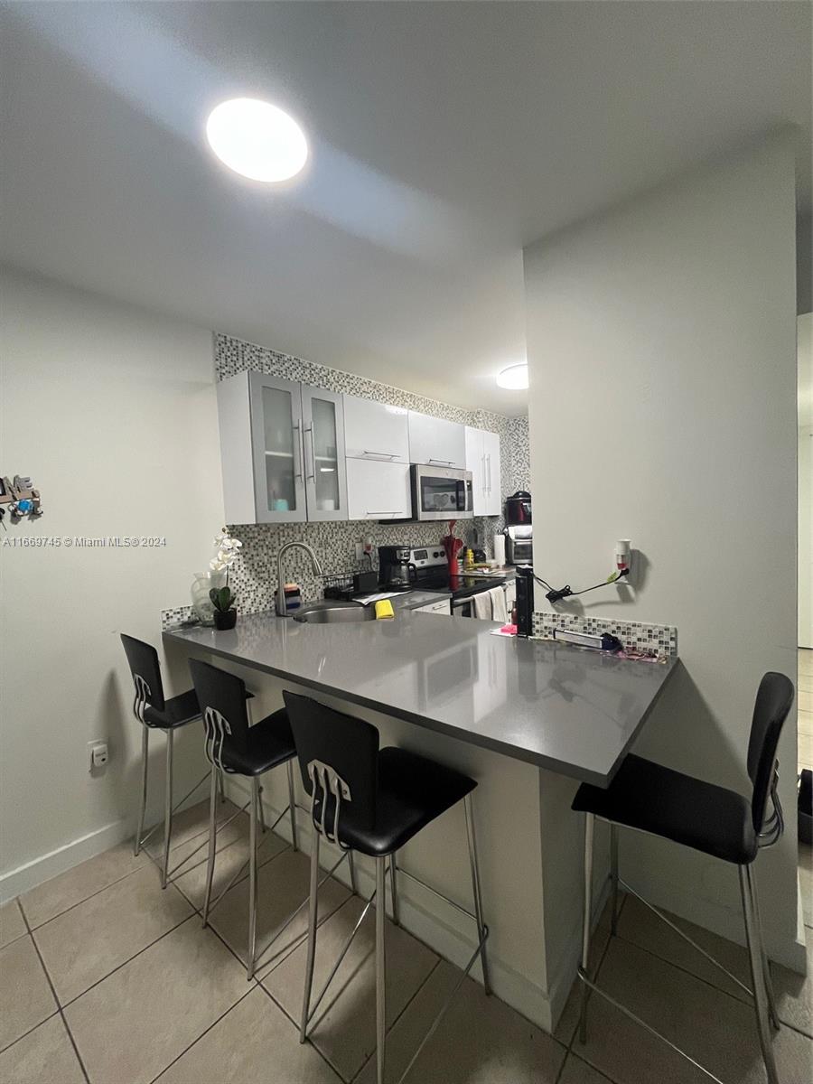 A kitchen features a gray breakfast bar, white cabinets, and a mosaic tile backsplash — 8075 NW 7th St # 109, Miami FL 33126, MIAMI, FL