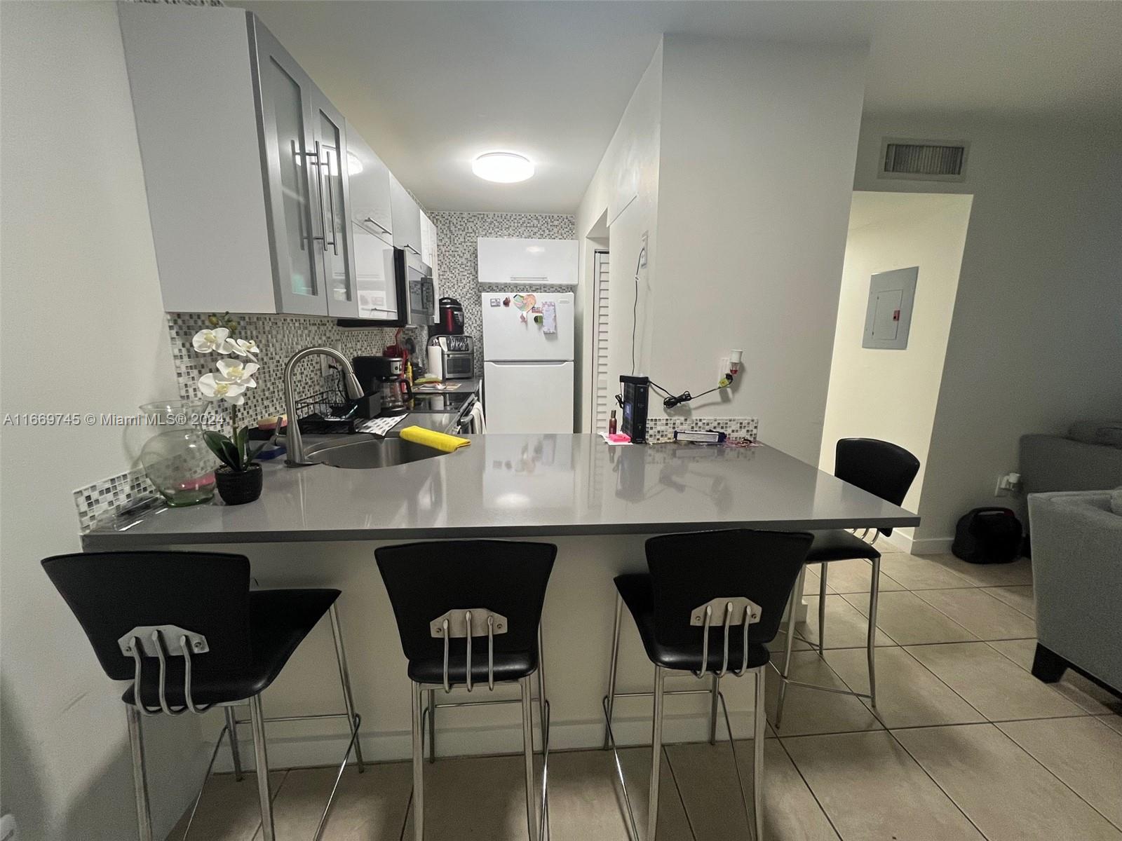 A kitchen features a gray countertop, black bar stools, and white cabinetry — 8075 NW 7th St # 109, Miami FL 33126, MIAMI, FL
