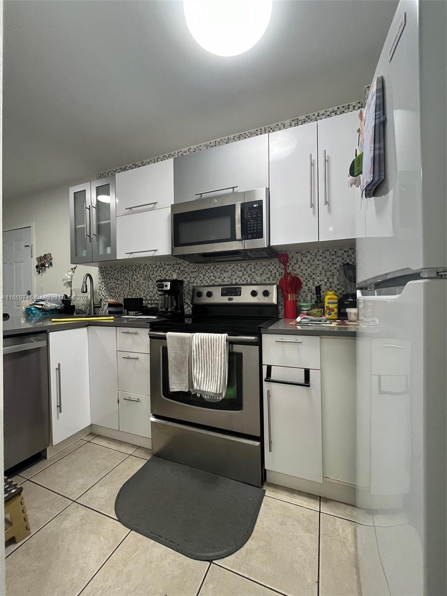 A kitchen features white cabinets, stainless steel appliances, and a mosaic tile backsplash — 8075 NW 7th St # 109, Miami FL 33126, MIAMI, FL