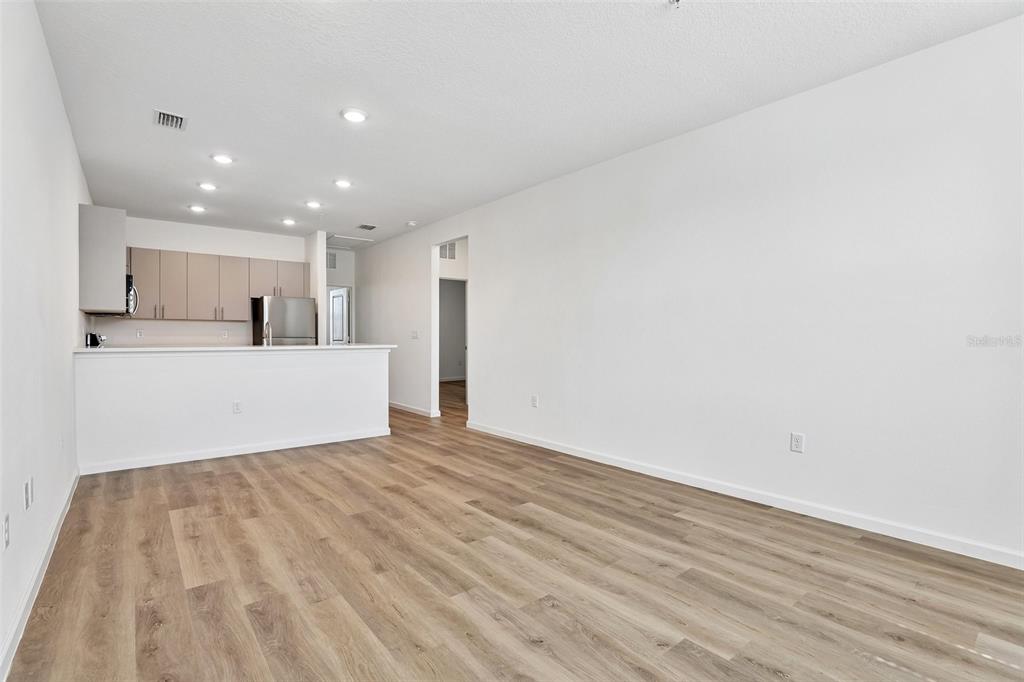 An open-concept living area features light wood-look flooring, white walls, and a kitchen peninsula — 3065 SOLDIER CITY WAY UNIT 101, ST CLOUD, FL