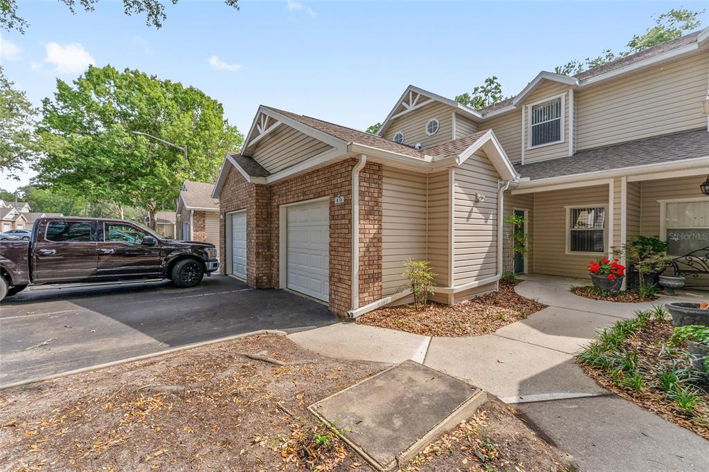 A two-story townhouse exterior features tan siding, brick accents, a two-car garage, and a walkway — 4700 SW ARCHER ROAD UNIT 13, GAINESVILLE, FL