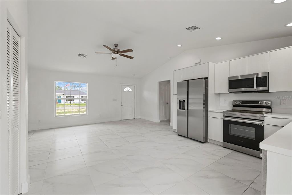 A bright kitchen and living area features white cabinetry, stainless steel appliances, and tiled floors — 107 ELBA DRIVE NE, LAKE PLACID, FL