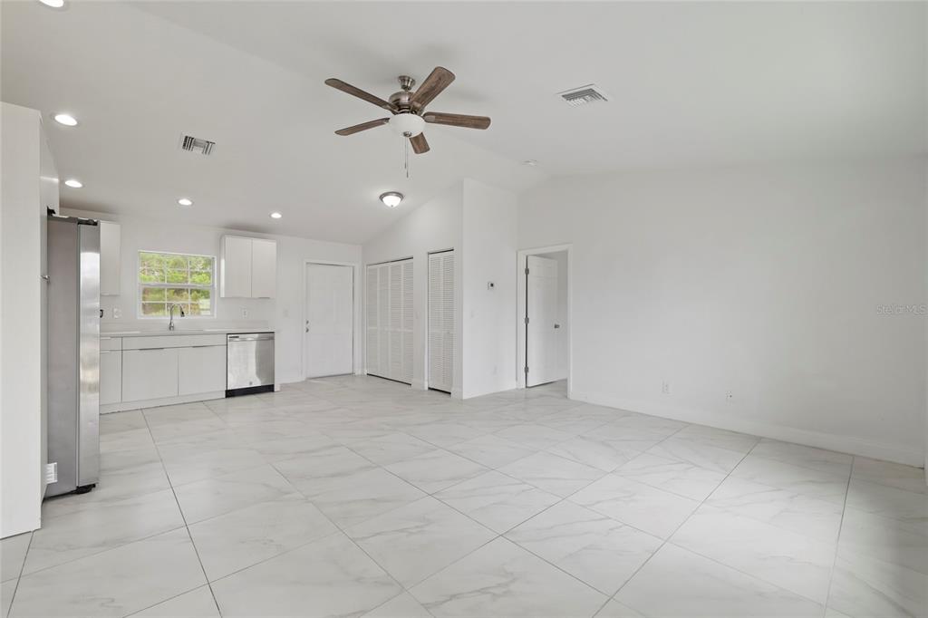 A bright, open-concept kitchen and living area features white cabinetry, stainless appliances, and tiled floors — 107 ELBA DRIVE NE, LAKE PLACID, FL