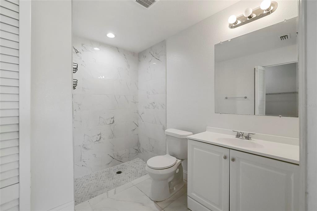 A bathroom features a walk-in shower with marble-look tile, a white vanity, and a toilet — 107 ELBA DRIVE NE, LAKE PLACID, FL