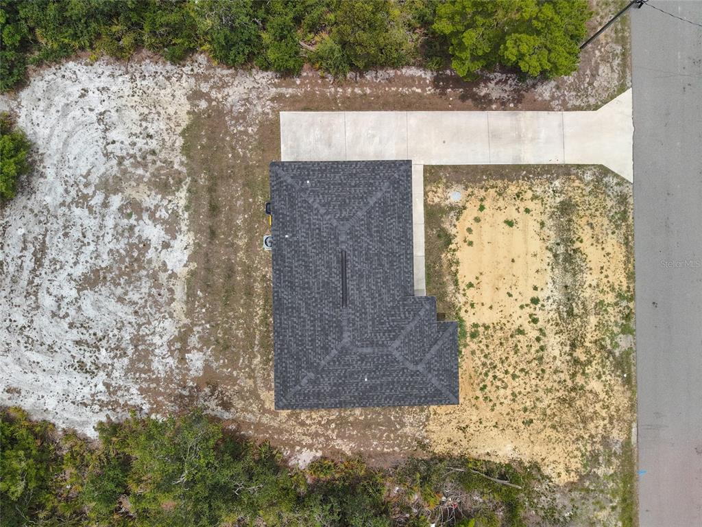 An aerial view shows a house with a dark roof, concrete driveway, and surrounding land — 107 ELBA DRIVE NE, LAKE PLACID, FL