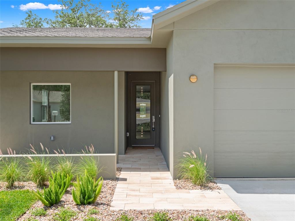 The exterior of a house features a paved walkway leading to a dark glass front door — 454 SKYFIELD COURT, LADY LAKE, FL