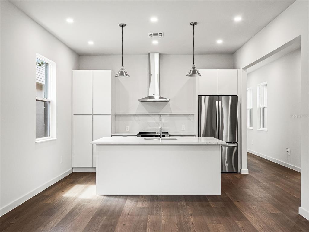 A modern kitchen features white cabinetry, a central island, stainless steel appliances, and wood flooring — 454 SKYFIELD COURT, LADY LAKE, FL