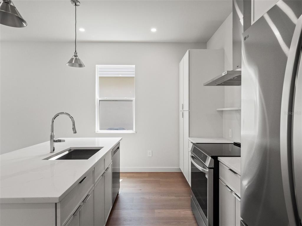 A modern kitchen features white cabinetry, a quartz island with a sink, and stainless appliances — 454 SKYFIELD COURT, LADY LAKE, FL