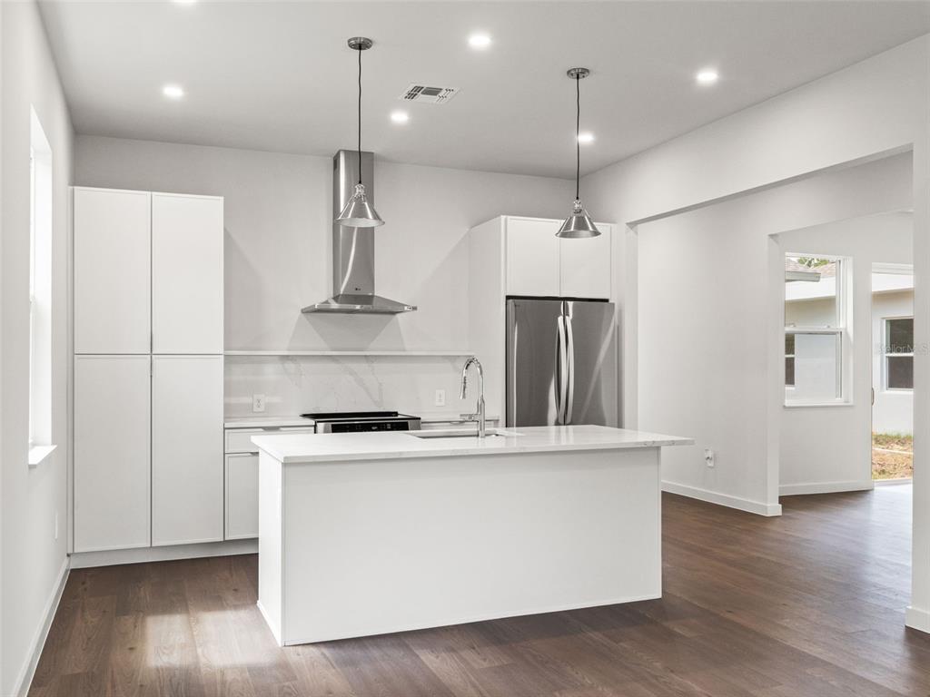 A modern kitchen features white cabinetry, a central island, stainless steel appliances, and wood flooring — 454 SKYFIELD COURT, LADY LAKE, FL
