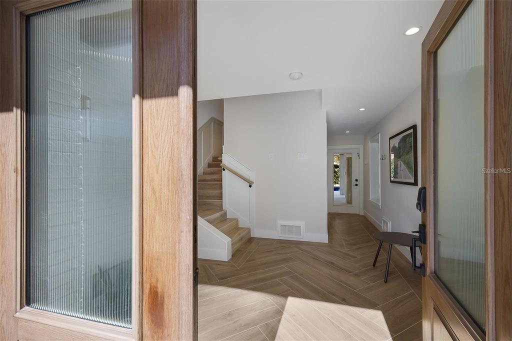 A view through an open wooden door into a foyer with herringbone-patterned wood-look flooring — 119 MCKINLEY DRIVE, SARASOTA, FL