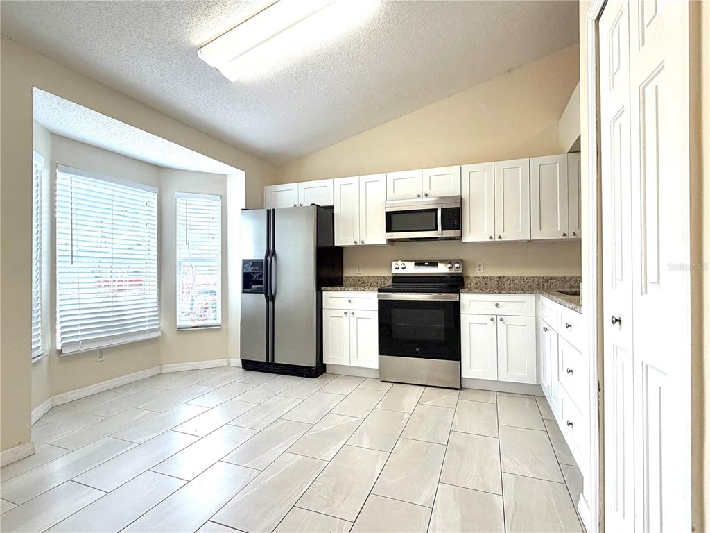 A kitchen with white cabinets, stainless steel appliances, granite countertops, and light-colored tile flooring — 1172 JADE EAST, KISSIMMEE, FL