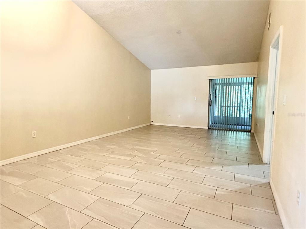An empty room features light-colored tile flooring, vaulted ceilings, and a sliding glass door — 1172 JADE EAST, KISSIMMEE, FL