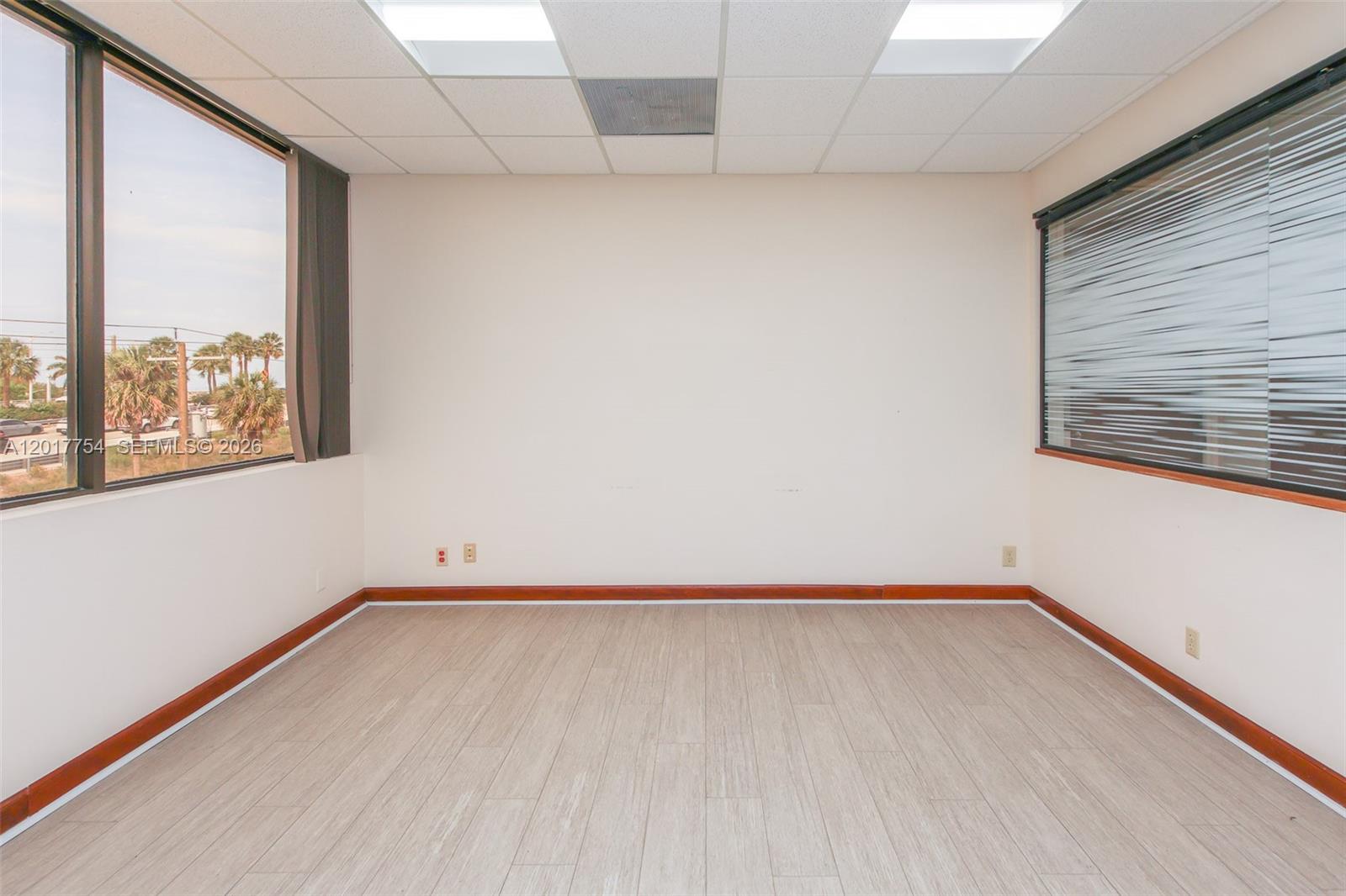 An empty office space features light wood-look flooring, white walls, and windows on two sides — 1900 Glades Rd # 245, Boca Raton FL 33431, BOCA RATON, FL