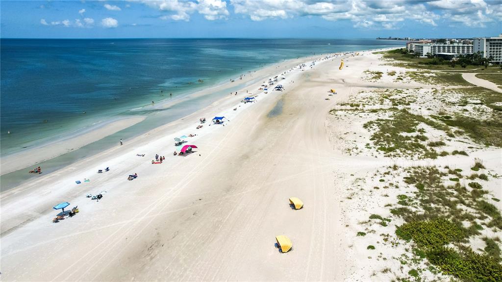 An aerial view of a sandy beach with scattered umbrellas and a hotel in the distance — 11605 GULF BOULEVARD UNIT 503, TREASURE ISLAND, FL