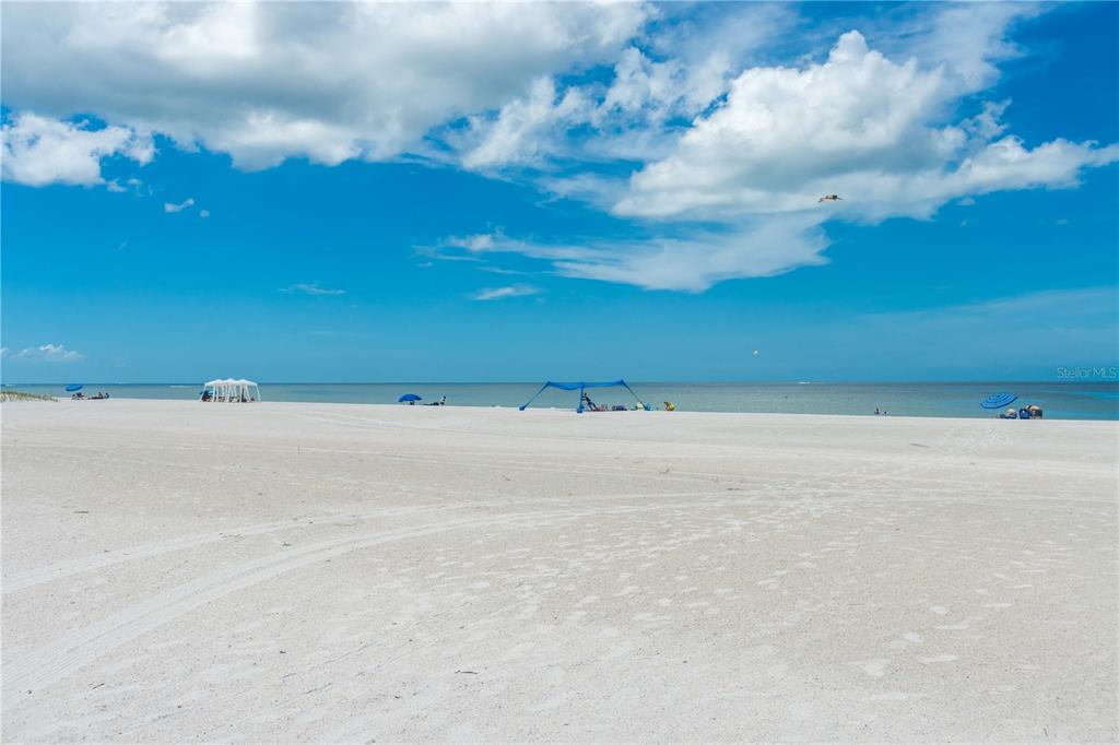 A wide, sandy beach stretches toward the ocean under a bright, partly cloudy blue sky — 11605 GULF BOULEVARD UNIT 503, TREASURE ISLAND, FL