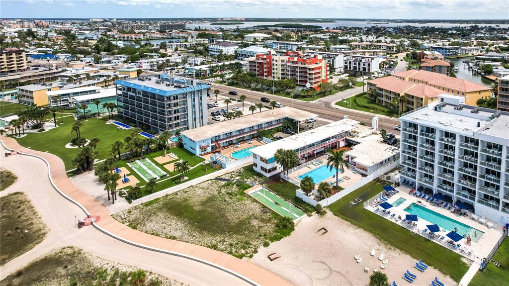 An aerial view shows multiple beachfront hotel buildings with swimming pools and a paved walkway — 11605 GULF BOULEVARD UNIT 503, TREASURE ISLAND, FL