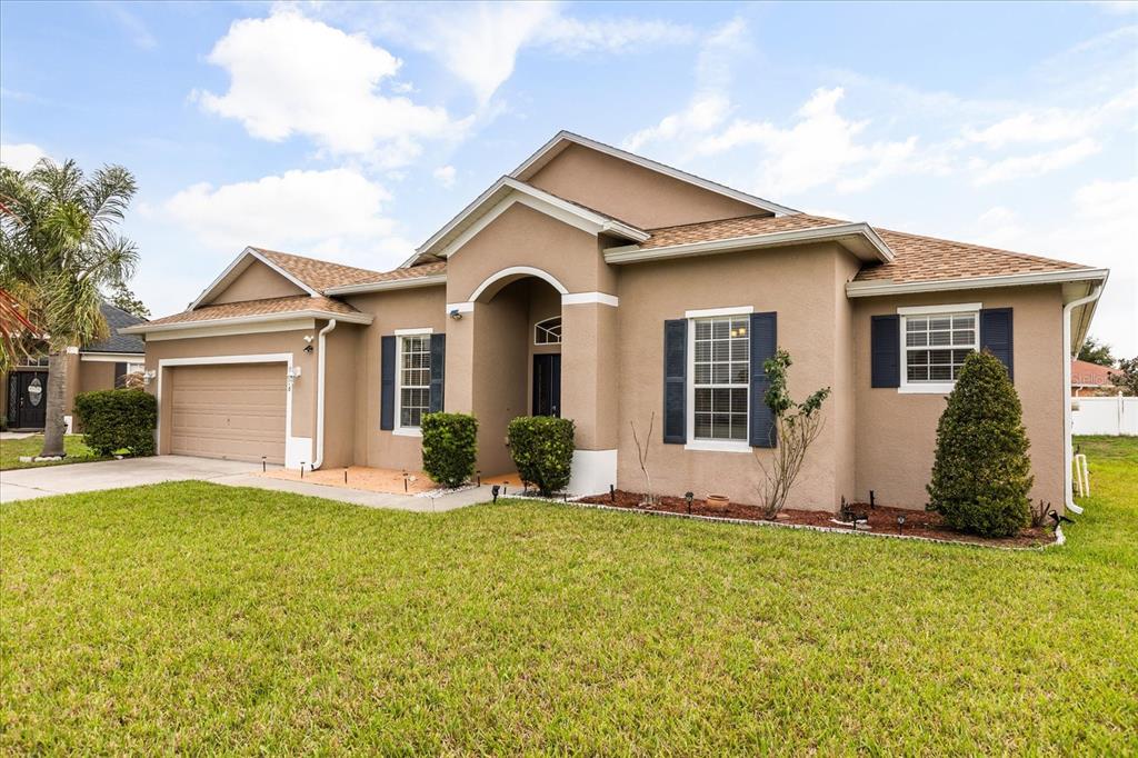 A single-story tan stucco house with a two-car garage and dark blue window shutters — 3878 WOOD THRUSH DRIVE, KISSIMMEE, FL