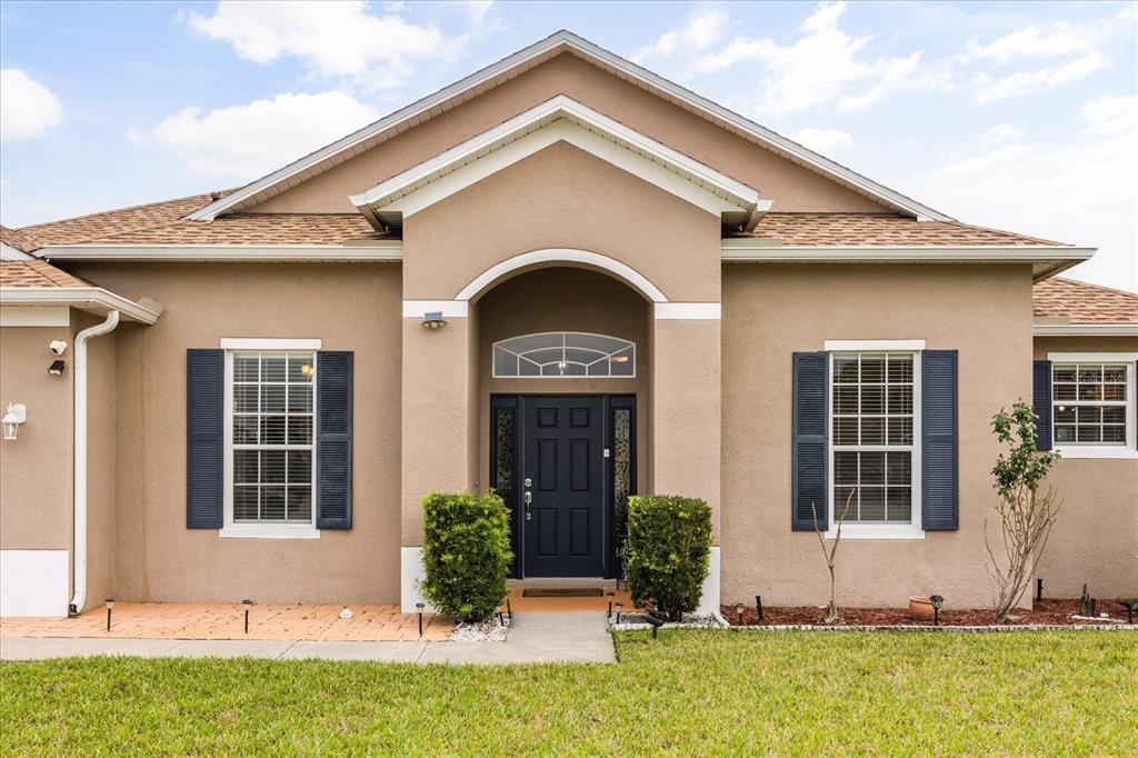 A tan stucco house features a dark blue front door, arched entryway, and blue shutters — 3878 WOOD THRUSH DRIVE, KISSIMMEE, FL