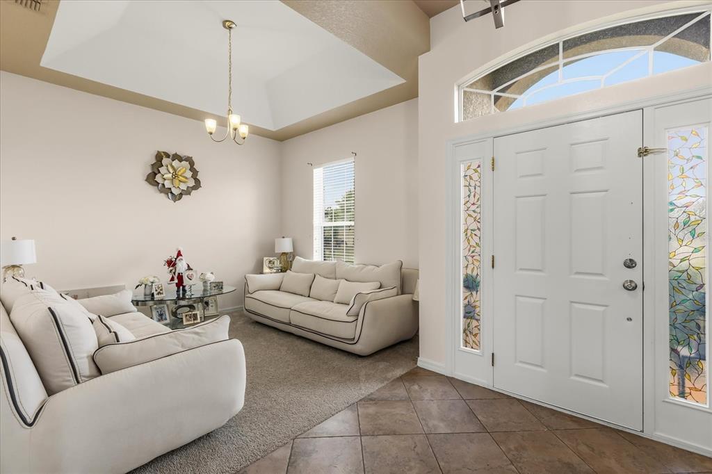 A living room with a vaulted ceiling, carpeted floor, and a white front door — 3878 WOOD THRUSH DRIVE, KISSIMMEE, FL