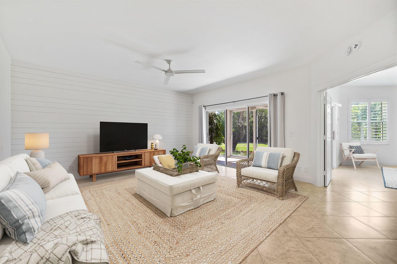 A bright living room features shiplap walls, tile flooring, wicker chairs, and a sliding glass door — 2703 N Fairway Dr Drive N, Jupiter FL 33477, JUPITER, FL