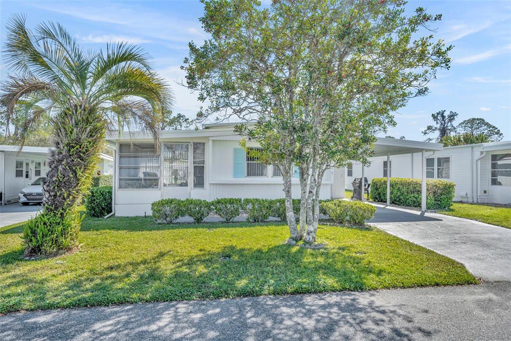 A single-story manufactured home with a screened porch, carport, and a large tree in front — 269 KELOU COURT, LEESBURG, FL