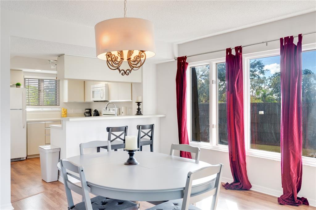 A dining area features a round table, chairs, a chandelier, and windows with red curtains — 1645 SPOONBILL LANE UNIT C, NAPLES, FL