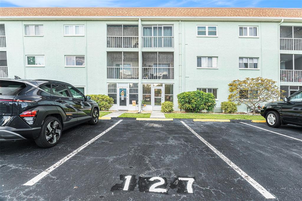 A three-story apartment building with a parking space marked 127 in the foreground — 801 83RD AVENUE N UNIT 127, ST PETERSBURG, FL