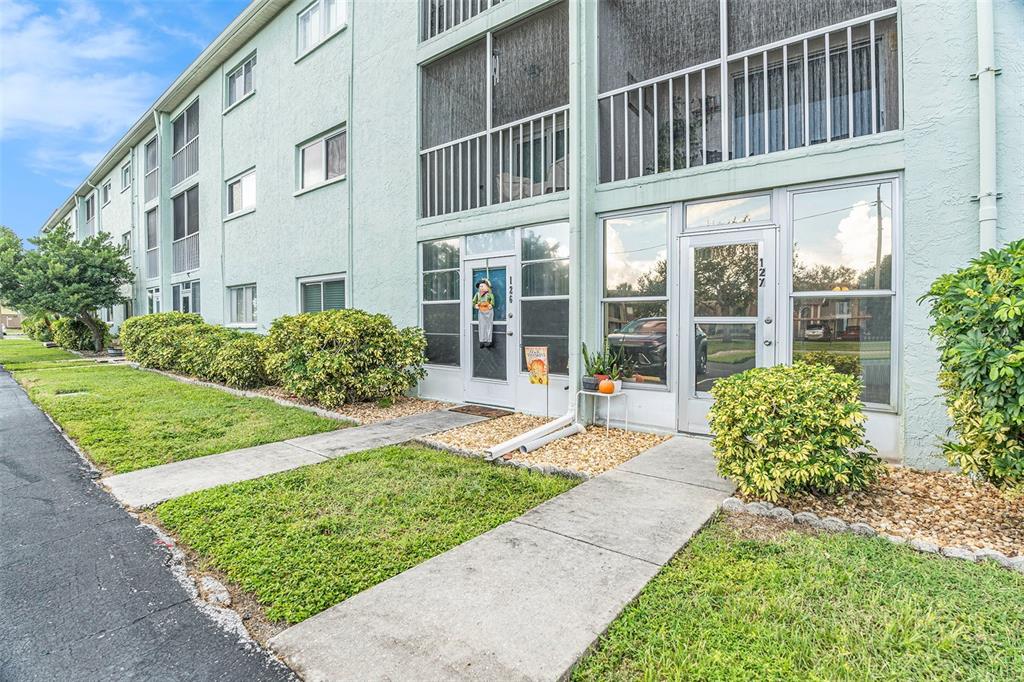 A light green multi-story apartment building features ground-level screened entryways and concrete walkways — 801 83RD AVENUE N UNIT 127, ST PETERSBURG, FL