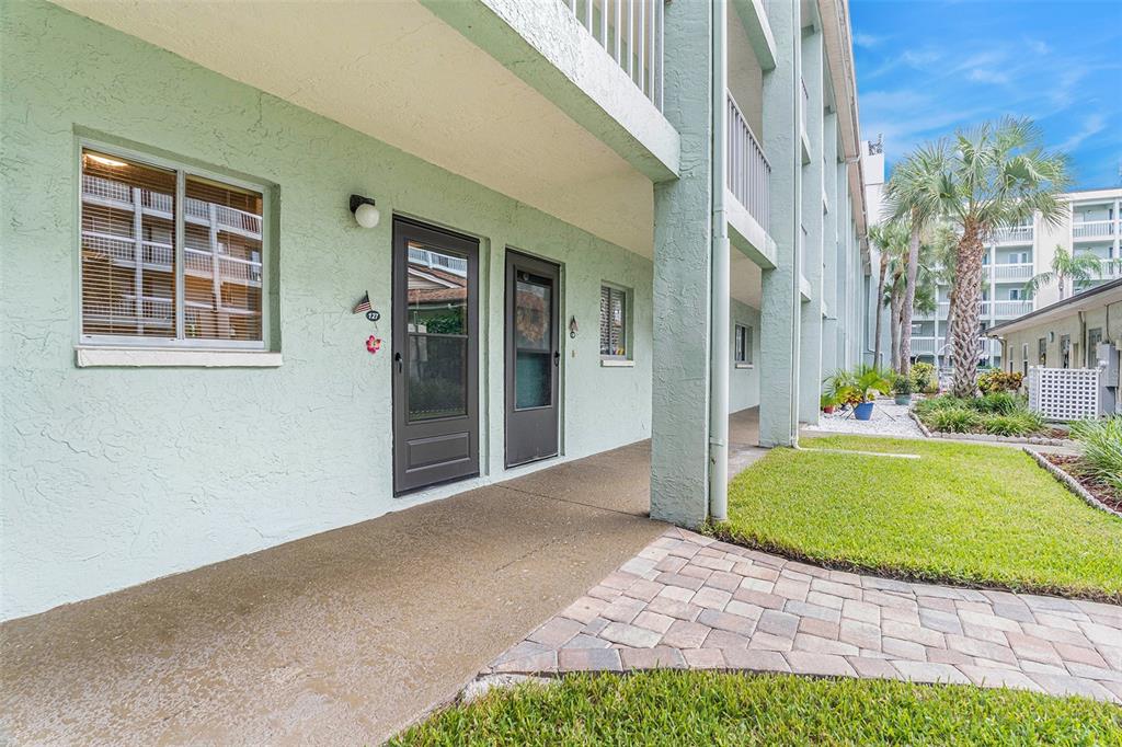 A ground-level apartment entrance with a paved walkway, green stucco walls, and two dark doors — 801 83RD AVENUE N UNIT 127, ST PETERSBURG, FL
