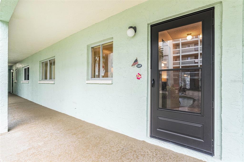 A light green exterior wall features a dark storm door, two windows, and unit number 127 — 801 83RD AVENUE N UNIT 127, ST PETERSBURG, FL