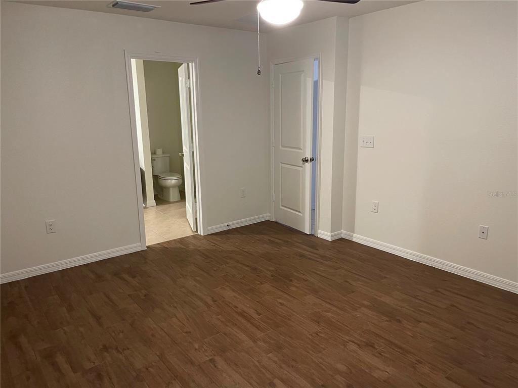 A bedroom with wood-look flooring, a ceiling fan, and two doorways leading to other rooms — 3063 SANCTUARY, CLERMONT, FL