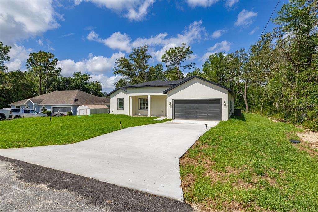 A modern, single-story house with a white stucco exterior and a gray two-car garage — 8100 N HILLVIEW CIRCLE, DUNNELLON, FL