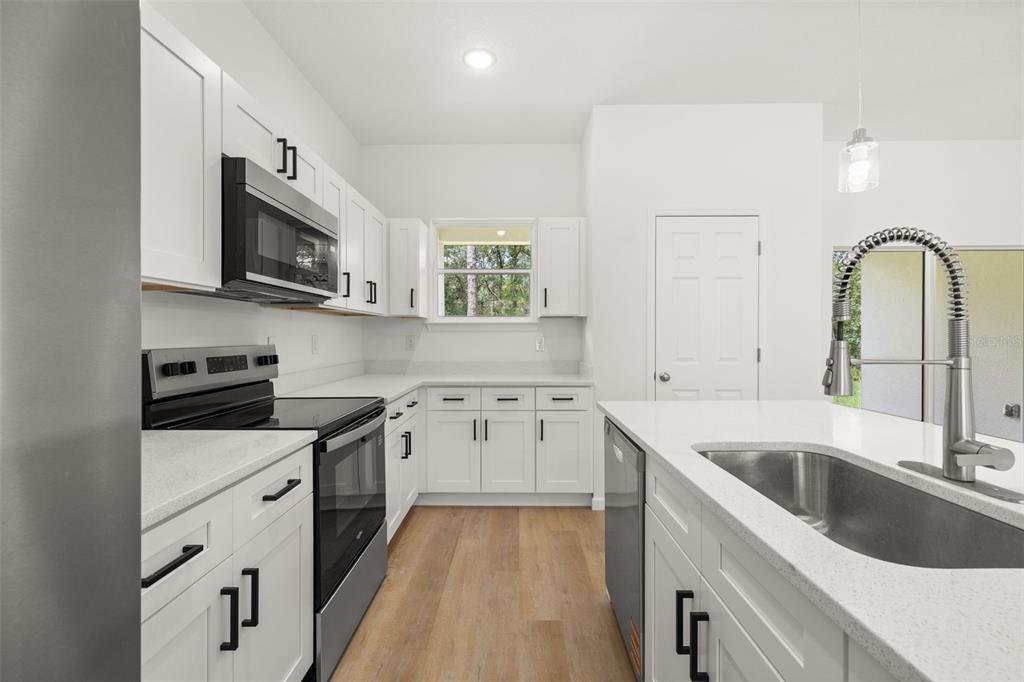 A modern kitchen features white cabinets, stainless steel appliances, a kitchen island, and light flooring — 8100 N HILLVIEW CIRCLE, DUNNELLON, FL