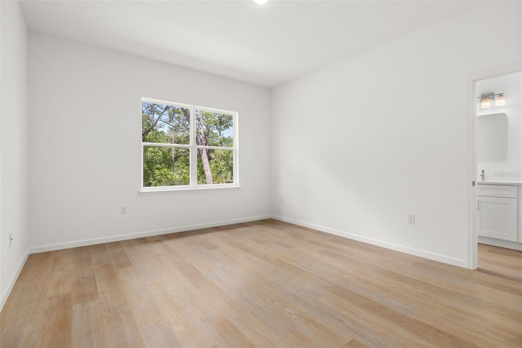A bright bedroom features white walls, light wood-look flooring, a window, and an attached bathroom — 8100 N HILLVIEW CIRCLE, DUNNELLON, FL