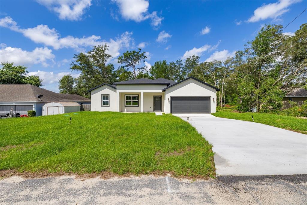 A modern, single-story white house with a dark roof and a two-car garage — 8100 N HILLVIEW CIRCLE, DUNNELLON, FL