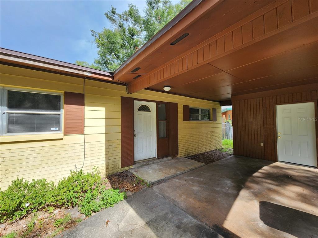 A yellow brick house exterior features a covered carport and two white entry doors — 2831 NE 17 DRIVE, GAINESVILLE, FL