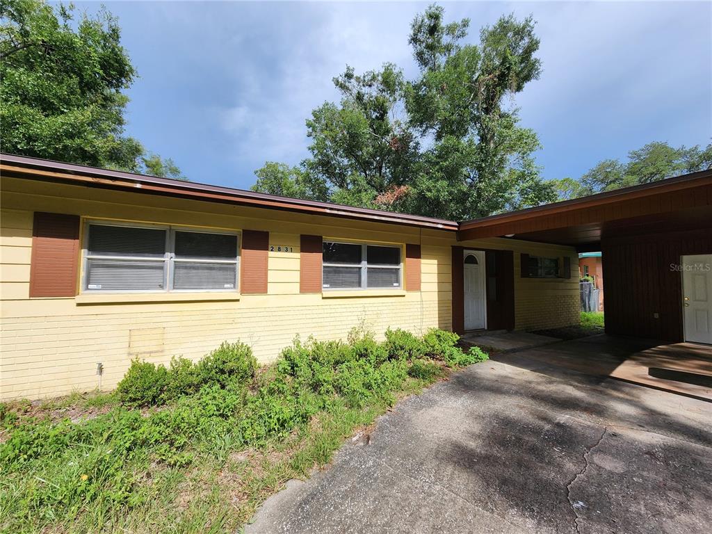 A yellow brick house features a carport, brown shutters, and a front entrance — 2831 NE 17 DRIVE, GAINESVILLE, FL