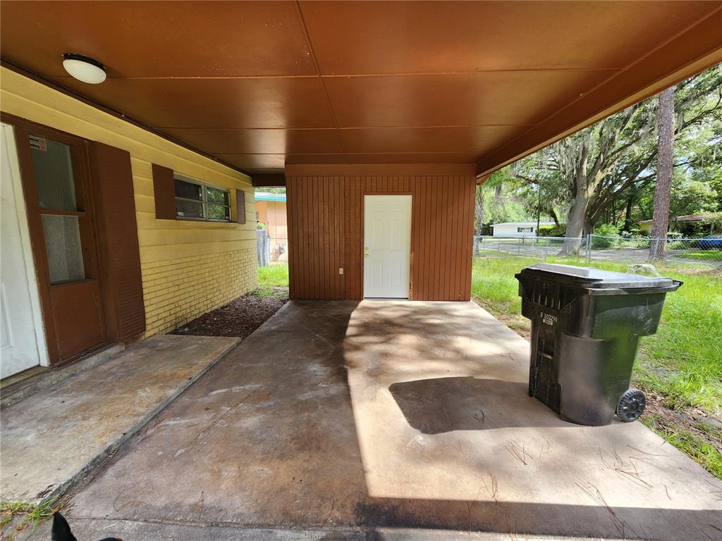 A concrete carport with a brown ceiling and a white door attached to a house — 2831 NE 17 DRIVE, GAINESVILLE, FL