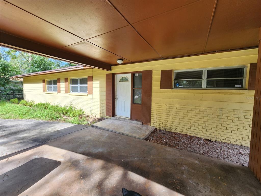 A yellow brick house features a covered concrete carport and a white front door — 2831 NE 17 DRIVE, GAINESVILLE, FL