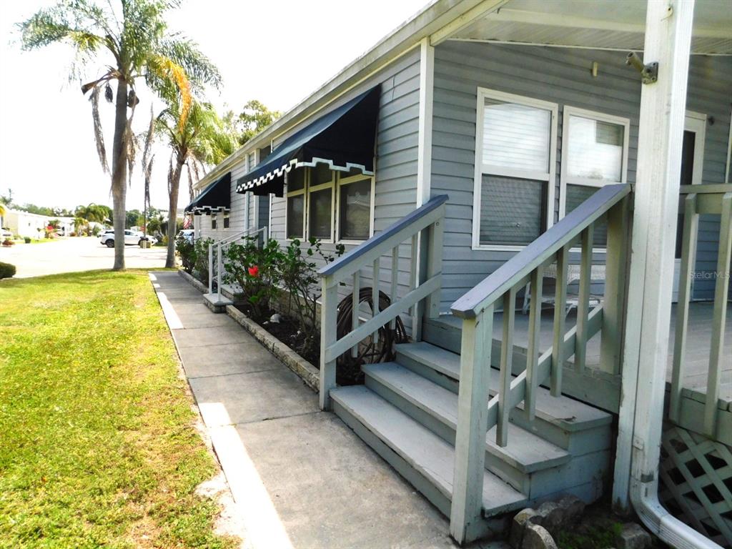 A light blue mobile home exterior features a concrete walkway, wooden stairs, and black awnings — 1001 STARKEY ROAD UNIT 395, LARGO, FL