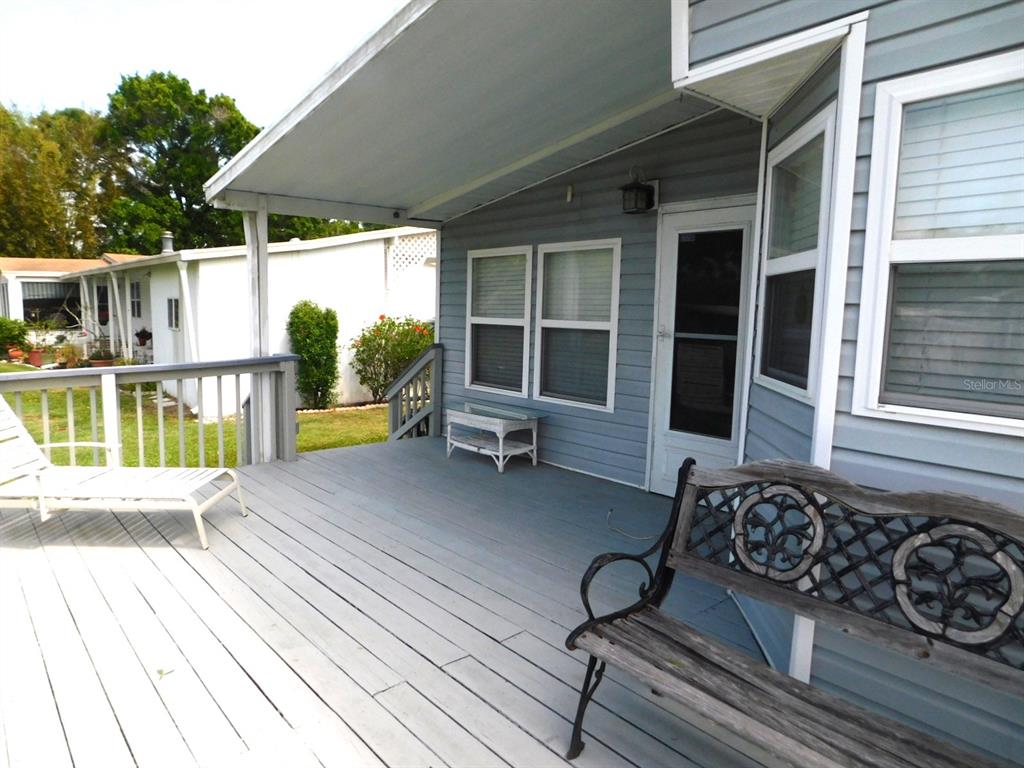 A gray wooden deck features a metal bench, a lounge chair, and a small table — 1001 STARKEY ROAD UNIT 395, LARGO, FL