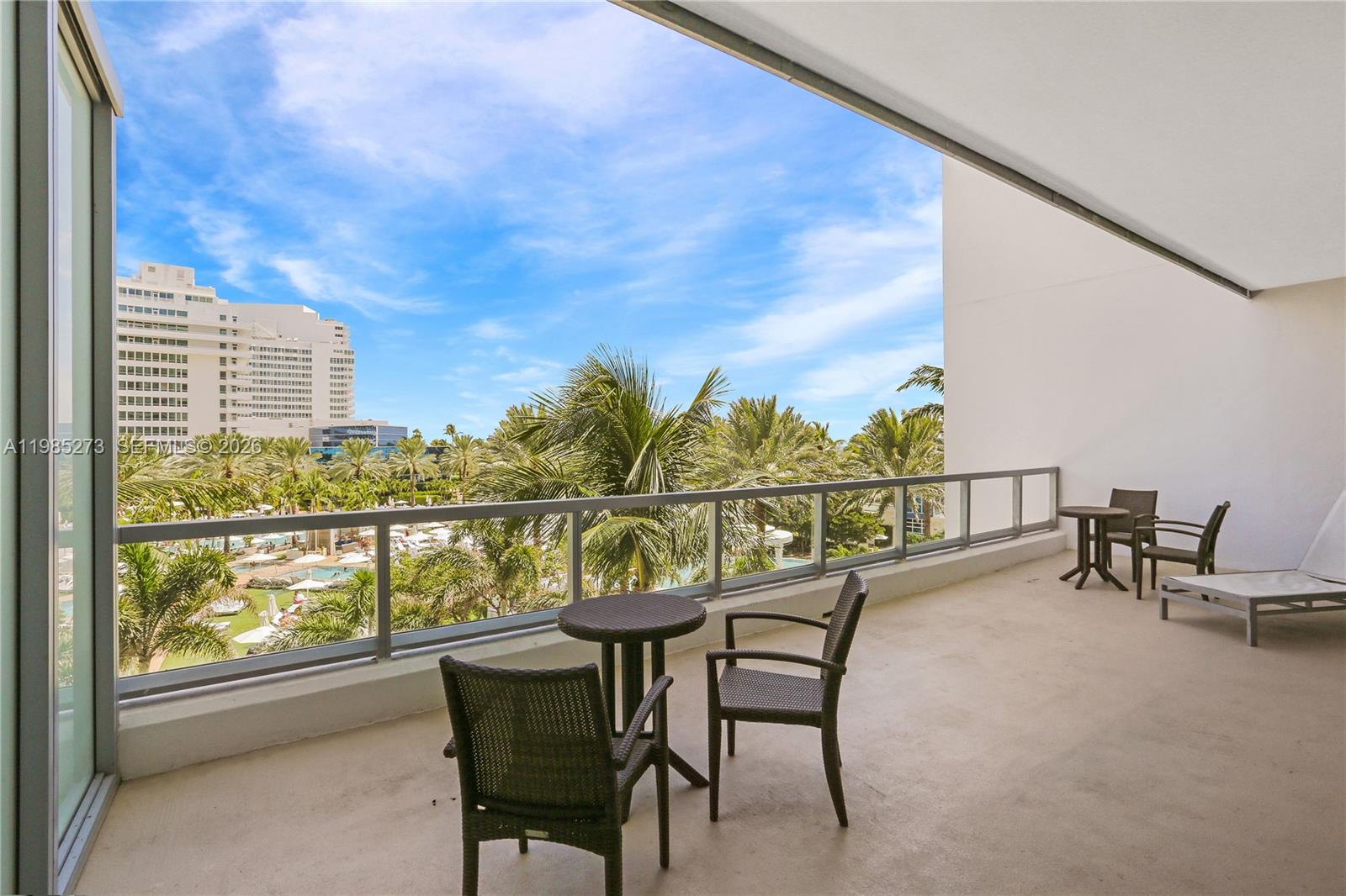 A balcony features outdoor furniture, a glass railing, and a view of palm trees and buildings — 4391 Collins Ave # 307, Miami Beach FL 33140, MIAMI BEACH, FL