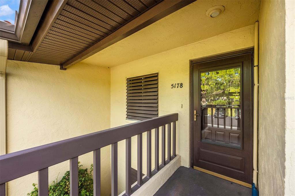 An exterior view of a building entrance with a brown door and a wooden railing — 5178 LAKE VILLAGE DRIVE UNIT 86, SARASOTA, FL