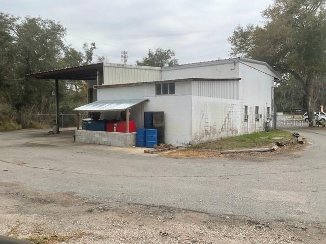 A white industrial building features a metal roof, a covered loading area, and exterior storage tanks — 32416 COUNTY ROAD 473, LEESBURG, FL